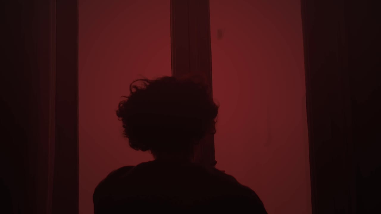 Man closing window under red light in tense alert atmosphere