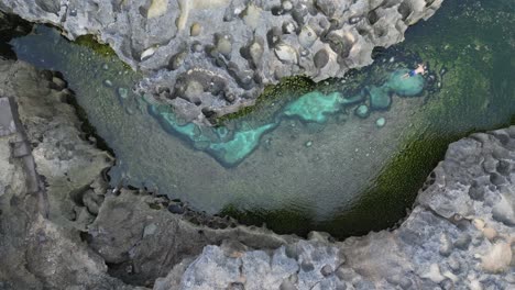 Man-swims-in-clear-turquoise-water-of-Angel's-Billabong-on-Bali-shore