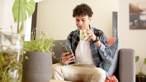 Biracial-Mann-Sitzt-Auf-Der-Couch,-Benutzt-Smartphone-Und-Trinkt-Kaffee-Zu-Hause,-Zeitlupe