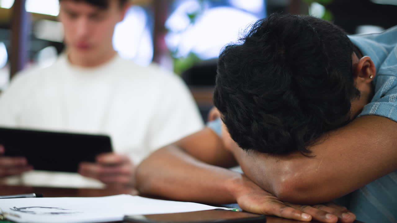 Closer view of lad with bob haircut leaning over wooden table supporting face with elbows conveying introspective mood in warm indoor light with blurred background capturing candid portrait moment