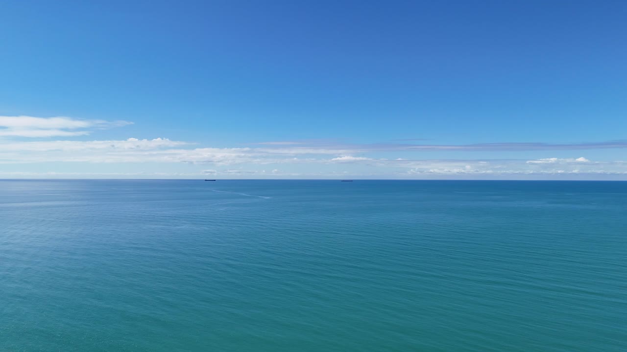 Drone glides over turquoise ocean, revealing sandy beach, lush rainforest, and clear blue sky