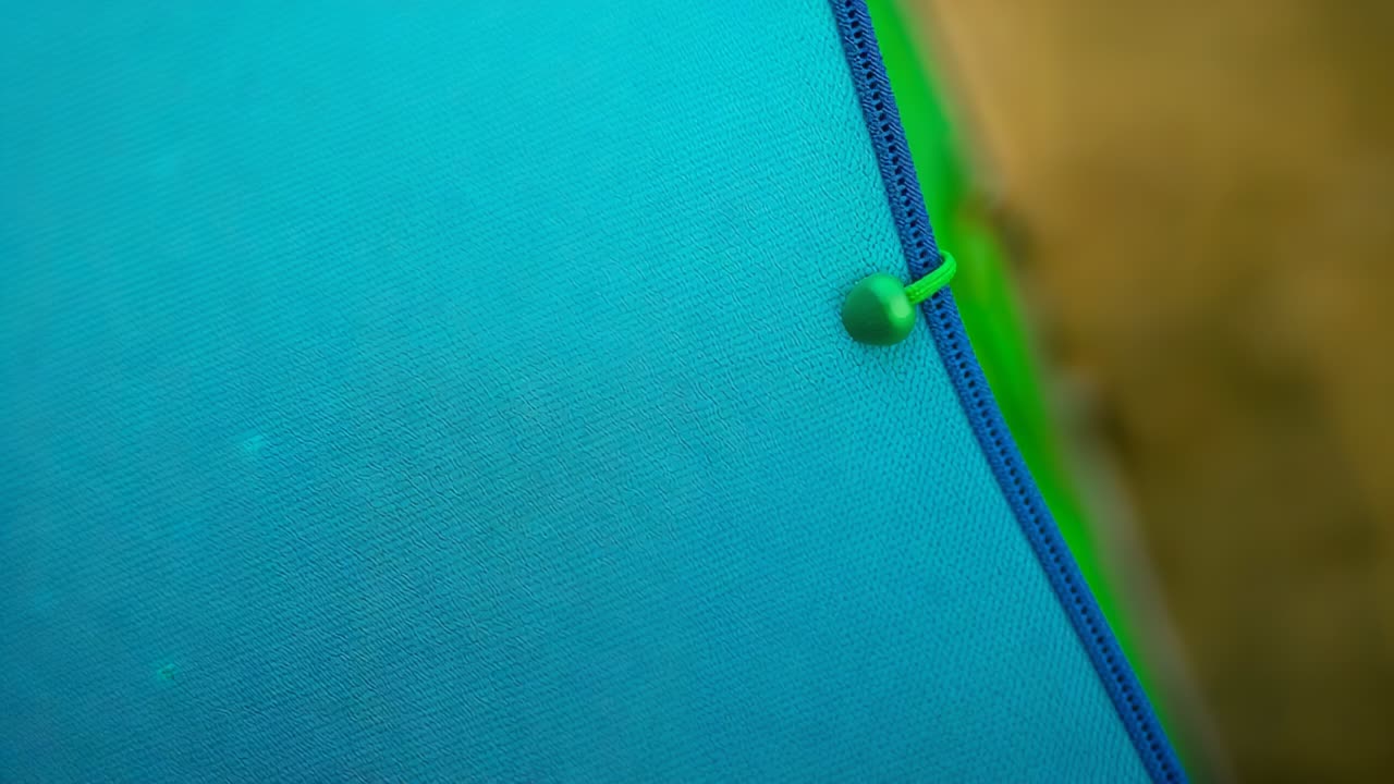 Gravação em close-up de um tecido azul, zíper azul e cordão verde com conta girando ao longo da costura