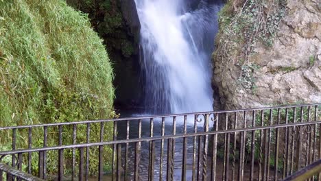 scenic splashing waterfall and metal guard railing between idyllic rock formation