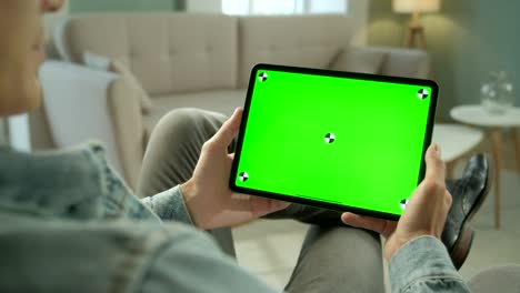 vista desde el hombro de un hombre sosteniendo y usando gestos con las manos en una pantalla de maqueta verde, una tableta digital sentada en una silla, un hombre comprando cosas o navegando por internet