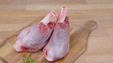 two lamb shanks with green herbs on wooden chopping board