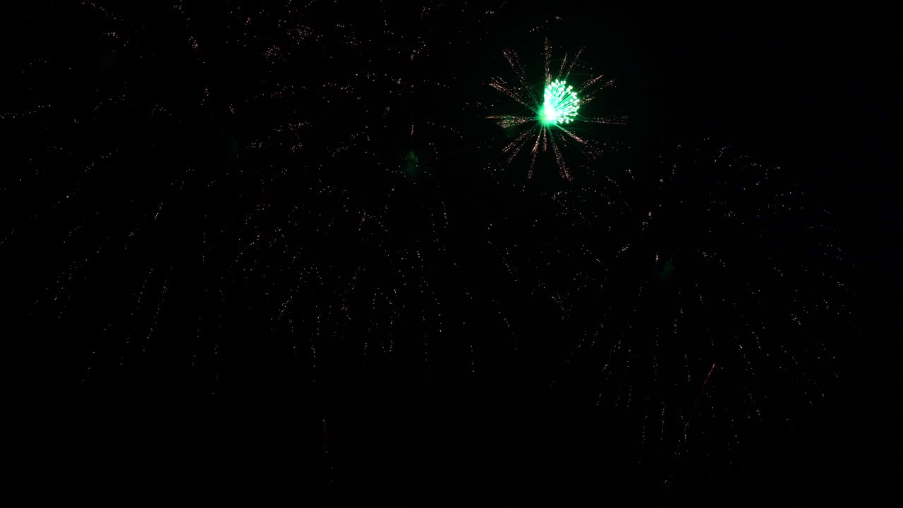 Fuochi d'artificio con il centro verde esplodono nel cielo notturno.