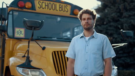 Thoughtful-bus-driver-standing-in-front-yellow-vehicle-looking-camera-close-up.