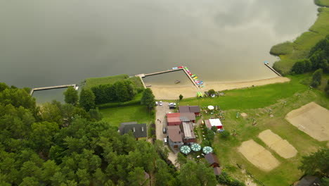 Luftüberflug-über-Hotelanlage-Mit-Privatem-Holzsteg-Für-Wassersportarten-Wie-Kajakfahren,-Kanufahren,-Tretbootfahren-Und-Fischerboote-Am-Ufer-Des-Hartowiec-Sees,-Polen