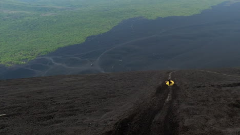 Woman-in-yellow-overalls-toboggans-down-volcanic-ash-slope,-Nicaragua