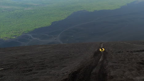 una mujer con un mono amarillo se arrastra por una ladera de ceniza volcánica, nicaragua.