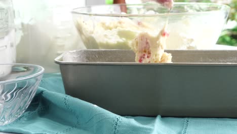 making a dessert called red raspberry tea cake made with fresh berries and vanilla buttercream frosting. great for tea parties. taking vanilla cake batter out of the bowl and putting into the pan