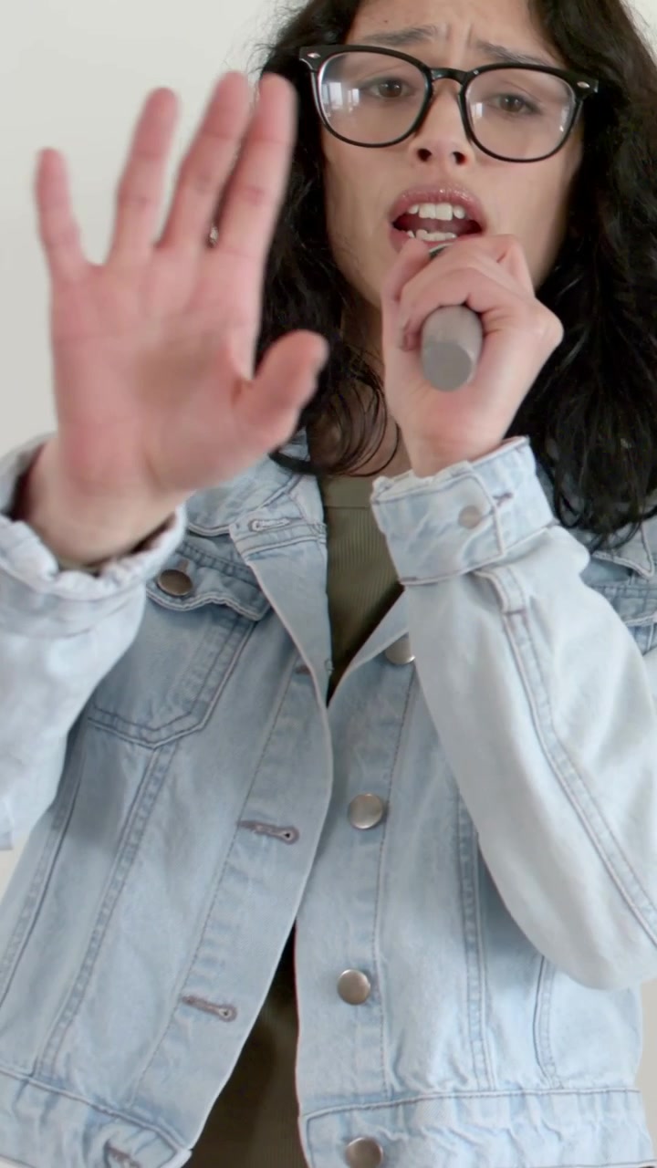 Vertical video: Camera panning lead singer in denim, specs singing, pointing with mic at session