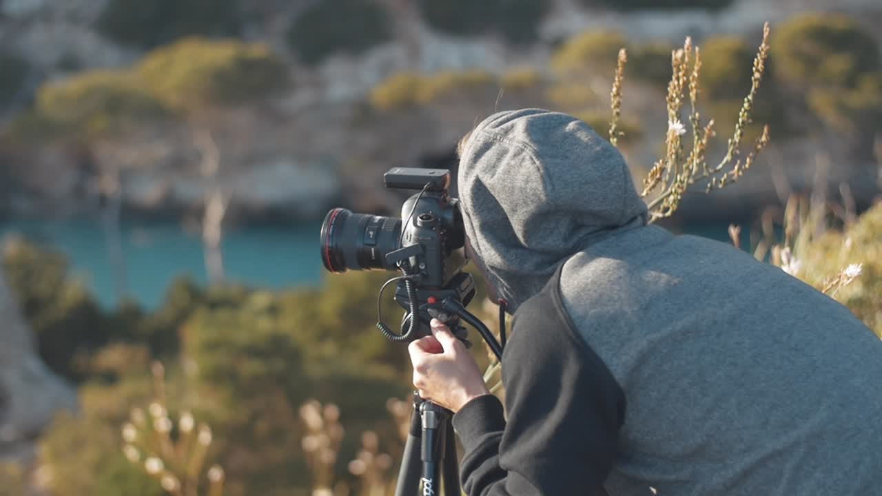 Photographer sets up his camera and looks through the finder of the camera on a tripod in a beautiful scenery at the bay "Calo des Moro" in the balearic island Mallorca, Spain - Slow Motion