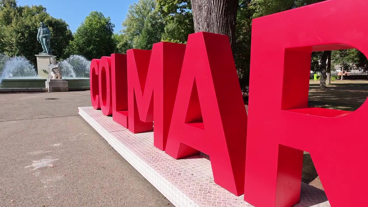 Cartel de bienvenida rojo para la ciudad de Colmar en la región de Alsacia, Francia, con una fuente histórica de fondo