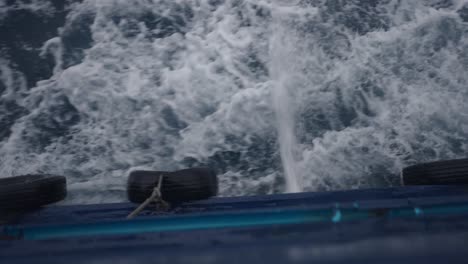 view from a boat's side showing churning ocean water and fender tires