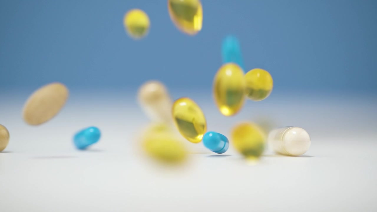 Macro ripresa 4K in slow motion di compresse e capsule vivaci e colorate che cadono su una superficie bianca, su uno sfondo blu con profondità di campo ridotta, creando un effetto cinematografico e dinamico.