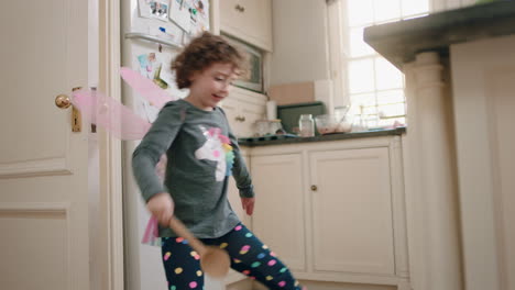 happy little girl dancing in kitchen wearing cute fairy wings having fun waving spoon playing pretend doing funny dance moves enjoying weekend at home