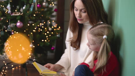 madre e hija sentadas en el suelo cerca del árbol de navidad