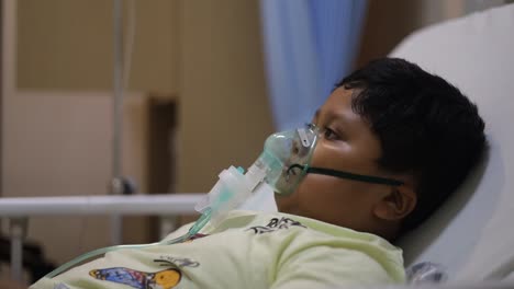 cute asian little boy with oxygen mask on her face on bed in the hospital room