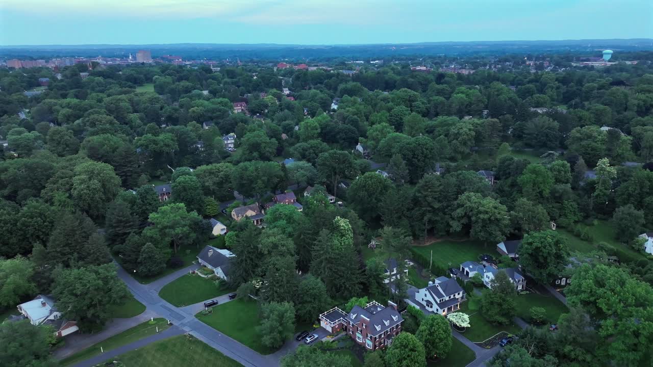 Ripresa aerea all'indietro di un quartiere di lusso con ville tra alberi verdi al tramonto
