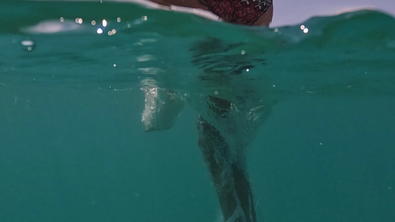 escena de vista trasera medio subacuática de mujer buceando en agua azul clara