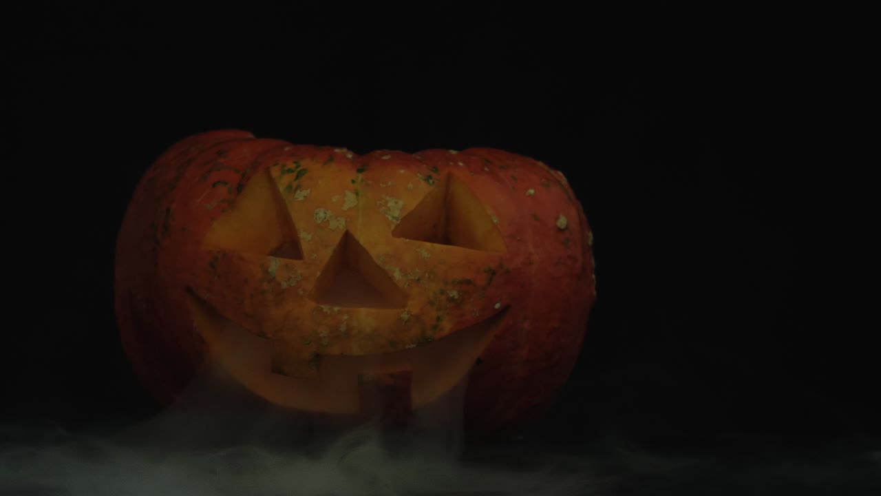 색 연기가 있는 어두운 테이블 위에 불이 인 할로윈 호박 잭 오 랜턴.