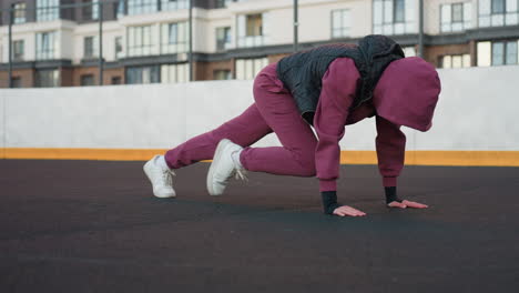 Driven female performing foot crawl exercise on urban court floor moving legs simultaneously with hands on ground showcasing core strength endurance and dynamic coordination outdoors
