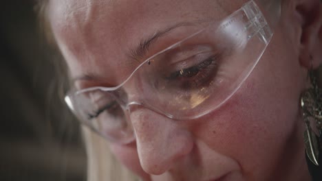 an extreme close-up on the face of a focused female worker. bright sparks from grinding are reflected in her protective safety glasses