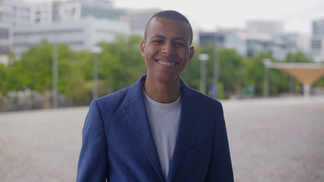 un uomo afroamericano sorridente che indossa un vestito blu in piedi all'aperto.