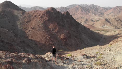 revealing aerial epic shot from drone of an young male standing on top of a rocky mountain in hatta, united arab emirates