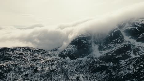 clouds and fog moving over mountain peaks partly covered with snow in winter in lofoten, norway. - aerial shot