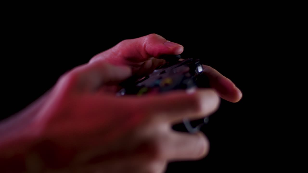 Playing video games in a darkened room with a black background close up on a controller joystick playing quickly