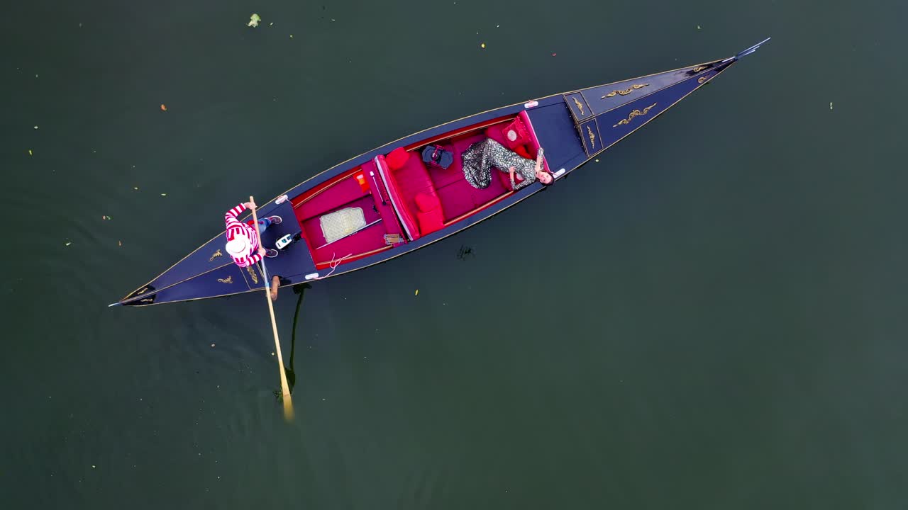 Luxury woman laying in gondola. Pretty girl travels in a boat in Venice. Gondolier managing a gondola on water. Camera rising up.