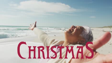 Animation-of-christmas-over-happy-senior-hispanic-woman-on-beach