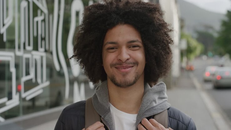 ritratto di un giovane sorridente che guarda la telecamera un allegro studente di sesso maschile che gode di uno stile di vita universitario di successo sullo sfondo della strada della città urbana