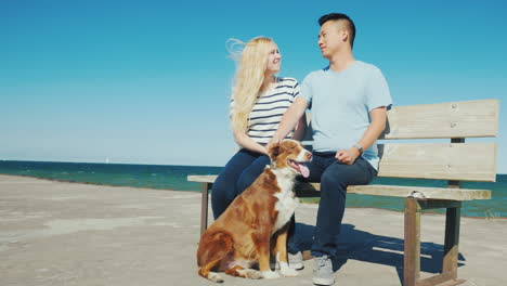 Una-Joven-Pareja-Está-Sentada-En-Un-Banco-En-El-Muelle-Jugando-Con-Su-Perro-Paseando-Con-Su-Mascota