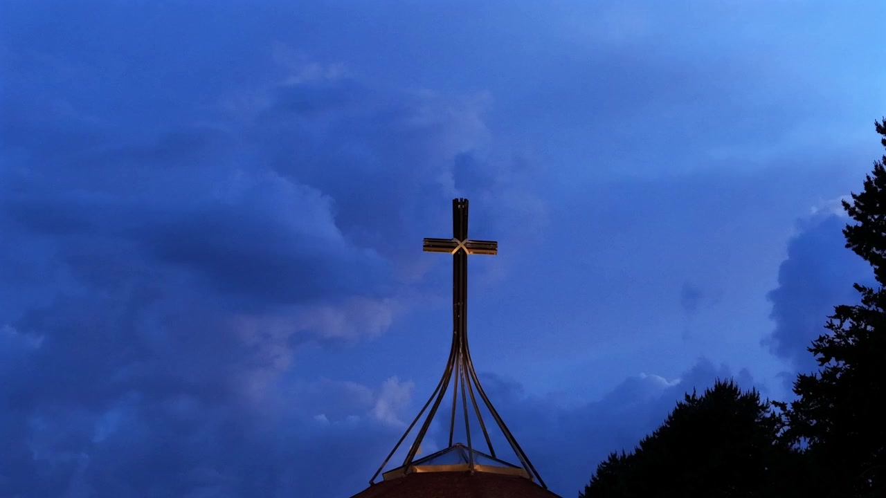 Een dramatische timelapse van een uniek, ingenieus ontworpen kruisbeeld dat afsteekt tegen een etherische lucht. Snel bewegende schemerwolken creëren een dynamische, stemmige achtergrond achter het religieuze symbool.