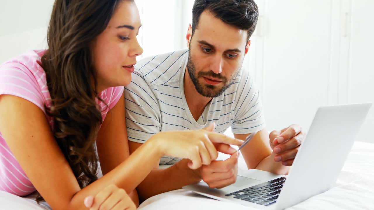 pareja haciendo compras en línea en una computadora portátil en el dormitorio