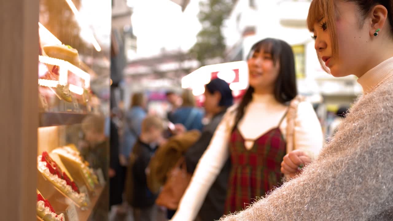 屋台の前に立つおしゃれな日本人友人二人が、デザートの選択肢について話し合っています。