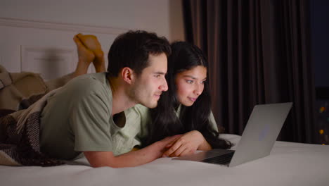 close up view of a couple watching interesting movie on laptop lying in bed at home 1