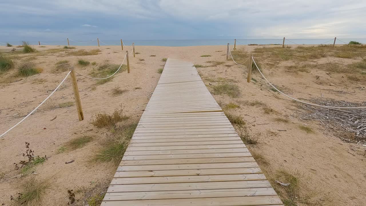 Wooden bridge over the sand direction to the beach walking in slow motion gimbal drone cloudy stormy day