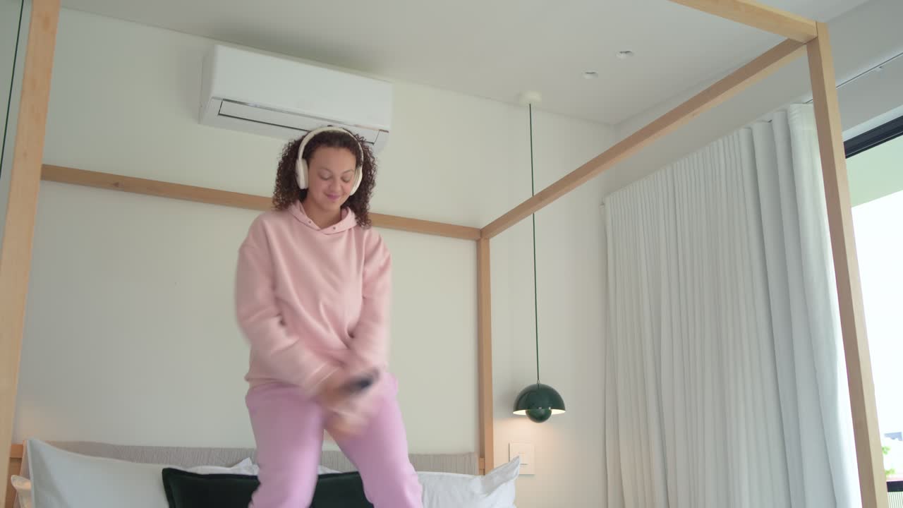 Music starting adult woman standing on bed dancing hopping grabbing phone and singing to match beat