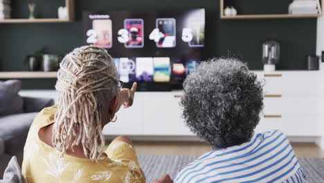 Senior-african-american-female-friends-on-couch-selecting-what-to-watch-on-tv,-slow-motion