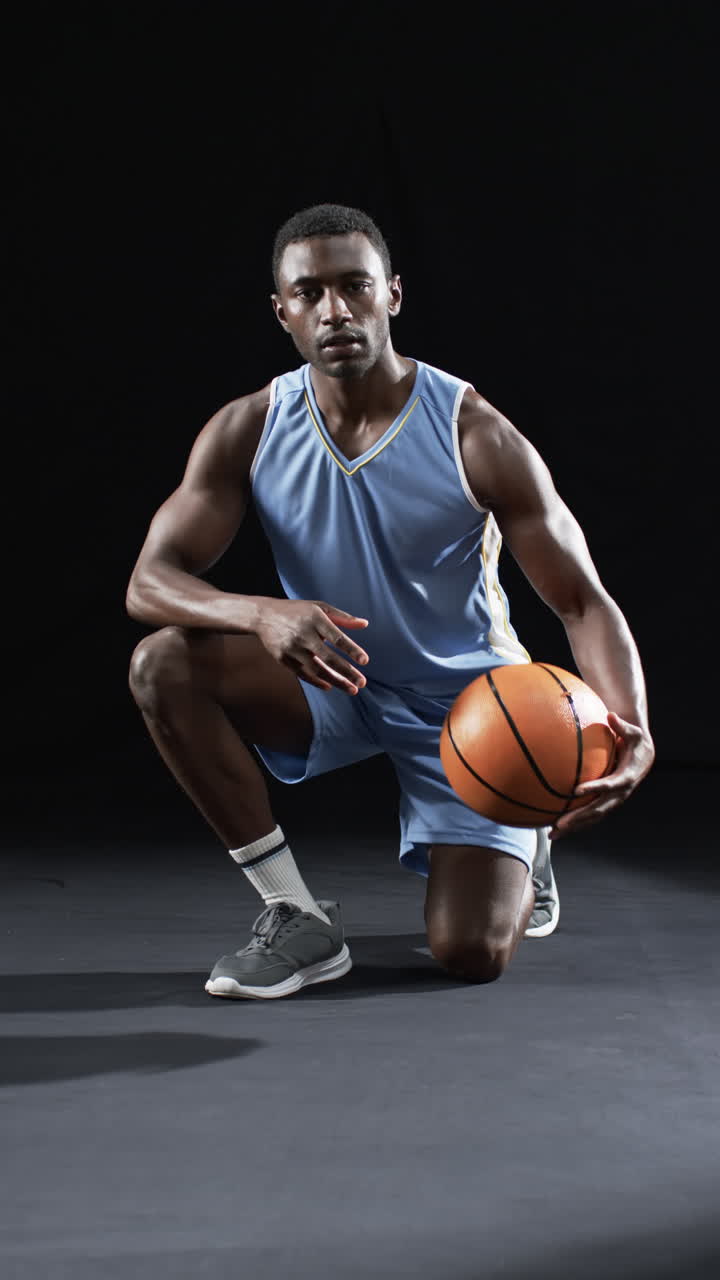 Vídeo vertical: Atleta masculino afro-americano posando com bola de basquete, fundo preto