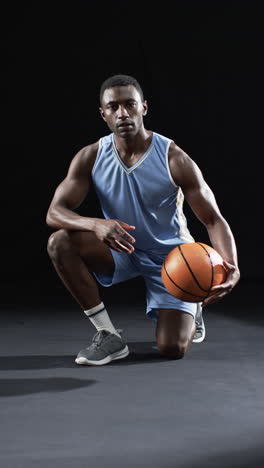 vertical video: african american male athlete posing with basketball, black background