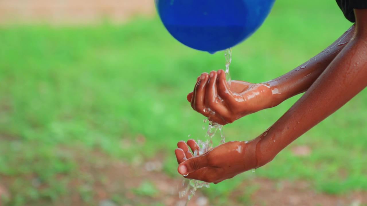 Kind wast handen onder stromend water, gestaag spoelen van handpalmen en polsen, blauwe wasbak druppelt erboven, gerichte hygiënepraktijk, buiten op grasveld, vreugdevolle opluchting en verfrissing, close-up detail.