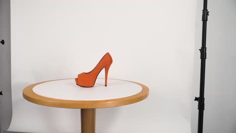 orange high-heel shoe on a wooden table in a photo atelier