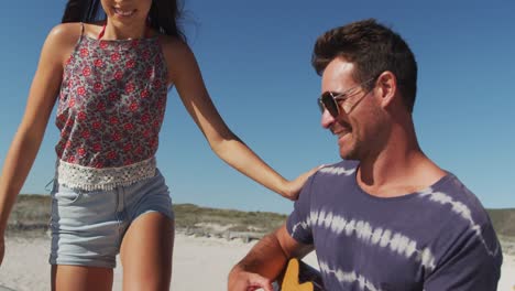 Feliz-Pareja-Caucásica-Sentada-En-La-Playa-Junto-Al-Mar-Tocando-La-Guitarra