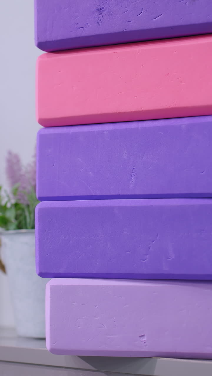 bloques de yoga de colores apilados en tonos de púrpura y rosa cuidadosamente dispuestos en el gabinete con un rodillo de espuma a juego y una planta en maceta en el fondo, creando un entorno de estudio de fitness calmante y organizado