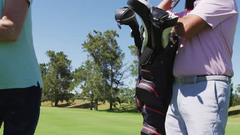 Kaukasisches-älteres-Paar,-Das-An-Einem-Strahlend-Sonnigen-Tag-Mit-Seinen-Golftaschen-Auf-Dem-Golfplatz-Spaziert